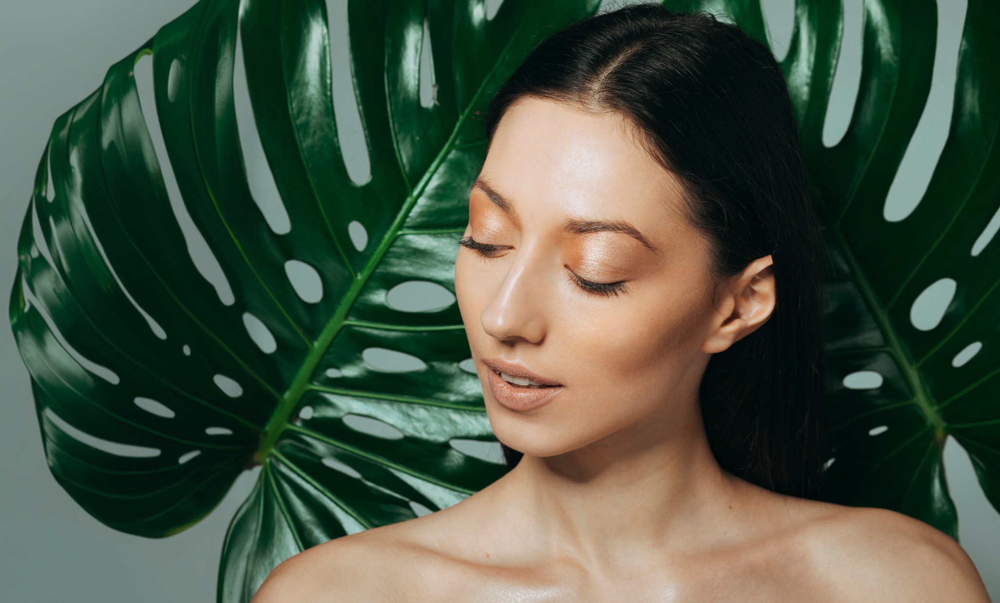 Model with radiant glass skin framed by tropical leaves