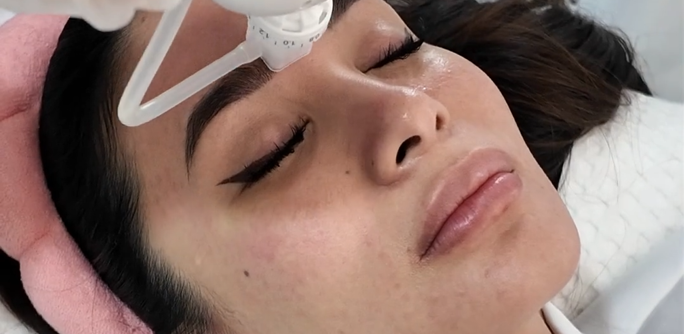 A client resting under a facial treatment device during an Aivee Dermashine session