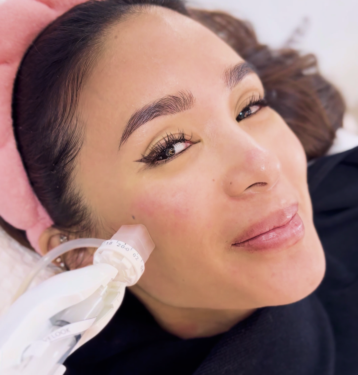 A smiling client with a pink headband receiving an Aivee Dermashine facial treatment
