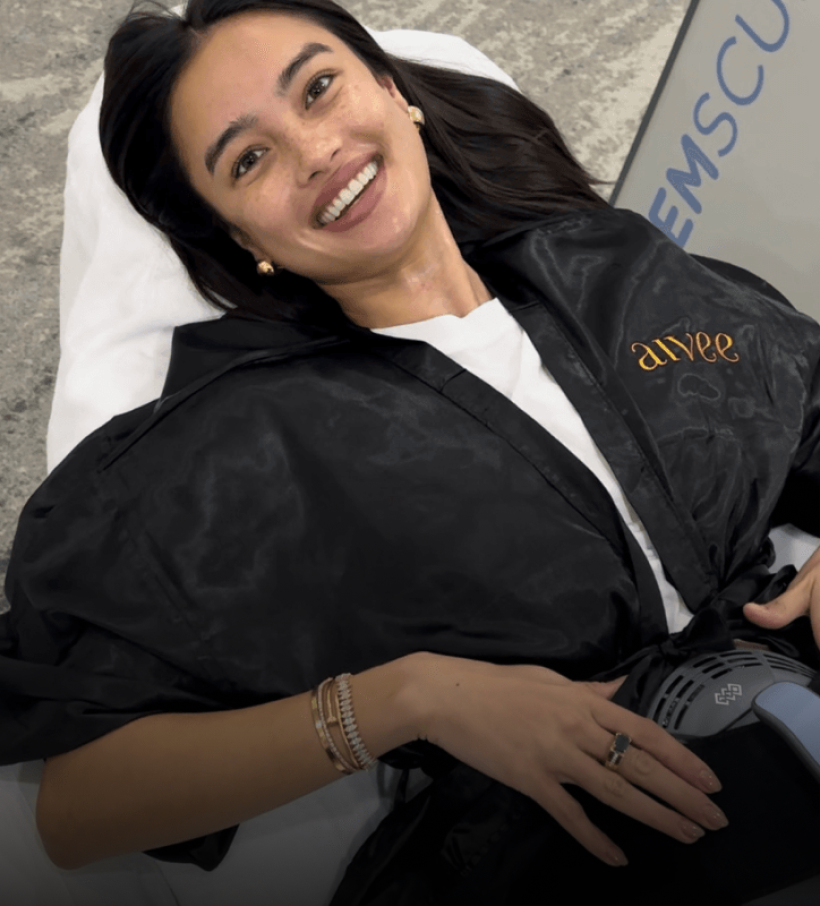 A smiling client in a black robe during an Aivee Emsculpt Neo body contouring session